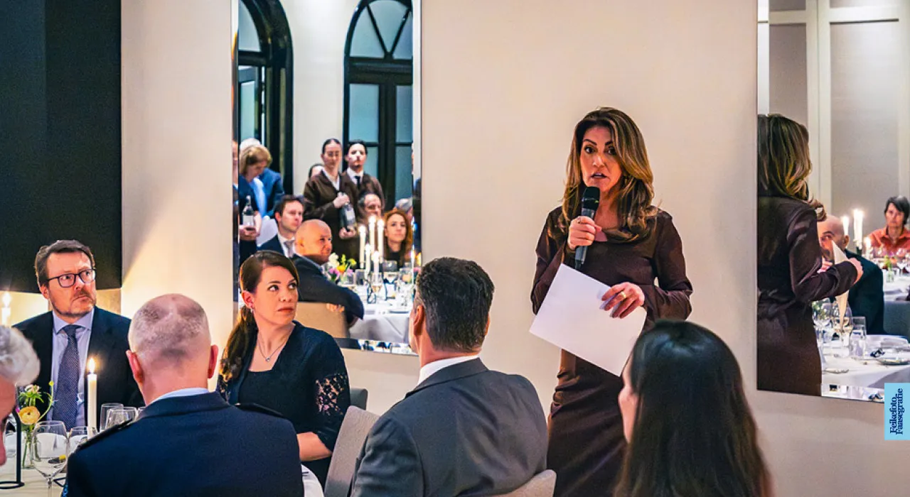 Dilan Yeşilgöz spreekt tijdens het exclusieve Captains-diner van het Ministerie van Defensie, voorafgaand aan het Space Symposium 2026. Links aan tafel luistert Prins Constantijn van Oranje-Nassau toe in een sfeervol verlichte dinerzaal."