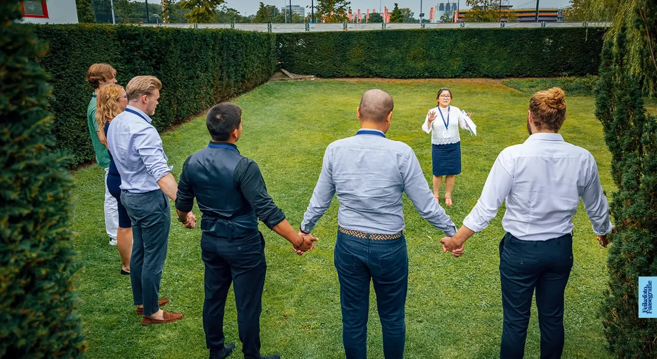 Een groep professionals staat hand in hand in een cirkel op het gras tijdens een teambuilding of outdoor workshop in de tuin van Villa Jongerius te Utrecht.